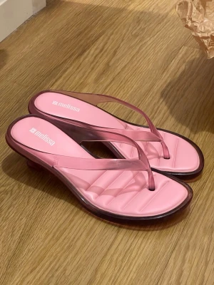 Rosa sandaler med klack från Melissa - Snygga rosa jelly kitten heels från Melissa med transparenta remmar och fyrkantig tå. Sandalerna har en låg klack och en vadderad sula för extra komfort. Tillverkade i plastmaterial som ger en modern och trendig look.