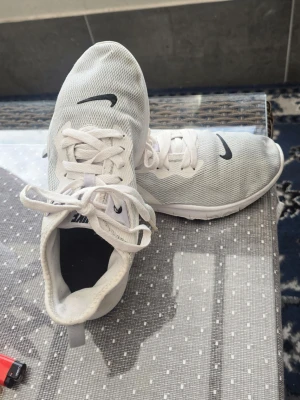 Vita Nike sneakers med mesh - Säljer ett par vita Nike sneakers med låg profil och svart swoosh på sidan. Skorna har ovandel i mesh för bra ventilation och klassisk snörning. Perfekta för en sportig och clean look.