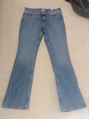 Blå bootcut jeans med 4 fickor - Säljer ett par klassiska blå bootcut jeans med fem fickor och normal midja. Jeansen har en lätt tvättad look och raka ben som går ut något nedtill. Tillverkade i denim med snygga sömmar och knappgylf. Perfekta för en avslappnad och trendig stil.