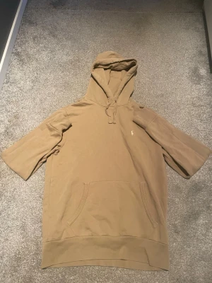 Beige hoodie - Stilren beige hoodie . Har en klassisk känguruficka framtill och en liten broderad logga på bröstet. Perfekt för en avslappnad och trendig look.