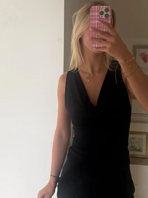 Svart ärmlös topp - Säljer en svart ärmlös topp med lös u-ringad hals. Toppen har en stilren och figurnära passform som ger en snygg siluett. Perfekt att matcha med jeans eller kjol för en trendig look.