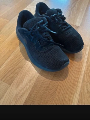 Svarta mesh sneakers nike med snörning - Snygga svarta sneakers med ovandel i mesh och klassisk snörning. Skorna har en låg profil och en diskret sula i svart. Perfekta för en sportig och avslappnad stil.