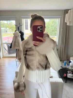 Vit pälsjacka med ribbade ärmar - Säljer en snygg vit pälsjacka med fluffig fuskpäls på överdelen och ärmsluten. Jackan har ribbade, långa ärmar och dragkedja framtill. Pälsen har inslag av gråbruna toner som ger en cool kontrast. Perfekt för dig som vill sticka ut i vinter!