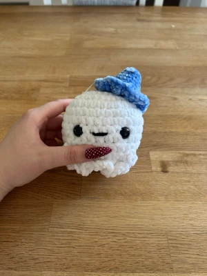 Virkad spöke med hatt - Söt handvirkad spöke i mjuk vit plysch med svarta säkerhetsögon. Spöket har en blå virkad hatt på huvudet och är perfekt som dekoration eller present. Liten och smidig att hålla i handen.