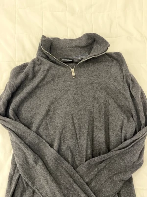 Grå stickad tröja från Jack & Jones - Mysig grå stickad tröja från Jack & Jones med halv dragkedja och hög krage. Perfekt för lager på lager och enkel att matcha med olika outfits. Tröjan har långa ärmar och är tillverkad i mjukt material.