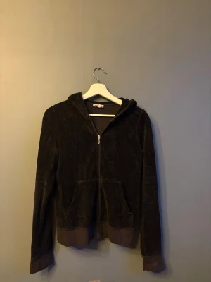Svart velour hoodie Juicy Couture - Mjuk svart velour hoodie från Juicy Couture med dragkedja framtill. Baksidan har ett stort rosa Juicy Couture-tryck. Hoodien har ribbade muddar och en klassisk huva. Storlek L men passar en S. 