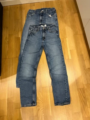 Blå raka jeans från H&M - Säljer ett par klassiska blå jeans med rak passform och fem fickor. Jeansen har normal midja, bälteshällor och snygga slitningar på låren för en avslappnad look. Perfekta till vardagsstilen och passar till det mesta.