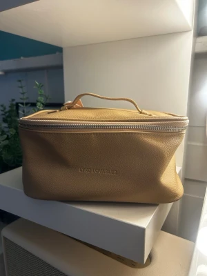 Beige necessär från Lyko - Snygg beige necessär från Lyko i mjukt konstläder med silverfärgad dragkedja och praktiskt handtag. Insidan är fodrad i matchande beige tyg och väskan har en boxig form som rymmer mycket. Perfekt för smink eller småprylar.