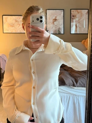 Vit långärmad skjorta från Zara - Klassisk vit skjorta från Zara med lång ärm och knappar framtill. Skjortan har en stilren, något figurnära passform och breda manschetter med knappdetalj. Perfekt till både jeans och kostymbyxor för en clean look.