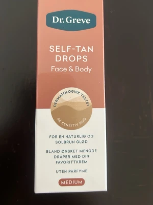  Dr. Greve Self-Tan Drops Medium – 30 ml - Självbruningsdroppar för ansikte och kropp från Dr. Greve. Dermatologiskt testad för känslig hud, parfymfri och ger en naturlig solbrun ton. Blandas enkelt med din favoritkräm. Förpackningen är i beige och vit med text i guld och vitt.