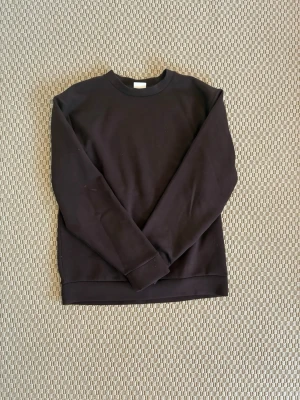 Brun basic sweatshirt - En enkel brun sweatshirt med rund hals och långa ärmar. Tröjan har en klassisk passform och ribbade muddar vid ärmslut och nederkant. Perfekt att matcha med jeans eller joggers för en clean look.