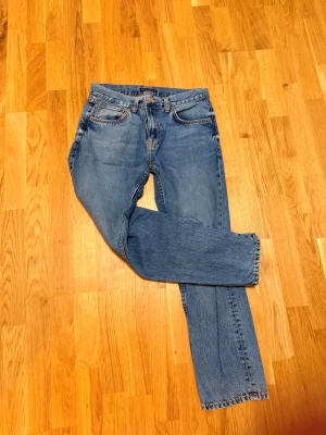 Nudie Blå raka jeans med fem fickor nudie jeans - Klassiska blå jeans i rak modell med fem fickor och normal midja. Jeansen har en tidlös tvätt och detaljer som metallknappar och nitar. Materialet är slitstark denim i bomull. Perfekta för en avslappnad och trendig look. Nudie jeans väldigt grisch stockholm stil är 32/30 men  passar mindre storlek