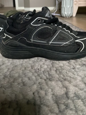 Svarta chunky sneakers med vita detaljer - Säljer ett par svarta chunky sneakers med vita linjer och CD-logga på hälen. Skorna har en robust sula och meshpaneler för extra ventilation. Snygg streetwear-look som sticker ut rengörs innan frakt pris kan diskuteras.
