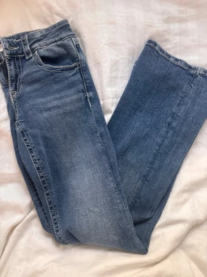 Blå jeans - Säljer ett par klassiska blå jeans med bootcut ben och tydliga vita kontrastsömmar. Jeansen har fem fickor och normal midja. Materialet är denim i bomull och de har en snygg tvättad look. Perfekta för en avslappnad och trendig stil.
