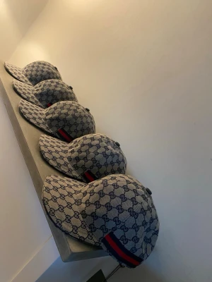 Bulk 4 kvar!! Guc@i  kepsar  - Säljer en klassisk Guc@i  keps i beige med blått GG-monogram över hela kepsen och en röd-blå rand på sidan. Kepsen har böjd skärm och justerbar rem bak. Tillverkad i Italien och fodrad med mörkblått tyg. Perfekt för dig som gillar exklusiv streetwear.