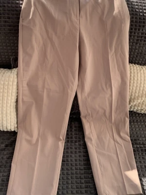 Beige raka kostymbyxor - Snygga beige kostymbyxor med rak passform och pressveck. Byxorna har hög midja och är tillverkade i ett slätt, vävt material som ger en stilren look. Perfekta för dig som vill ha en clean och modern stil.