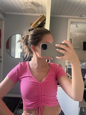 Rosa croppad ribbad topp med snörning - Säljer en rosa croppad topp med ribbad struktur och v-ringning. Toppen har korta ärmar och snygg snörning framtill som ger en trendig look. Perfekt för dig som gillar färg och vill sticka ut lite extra.