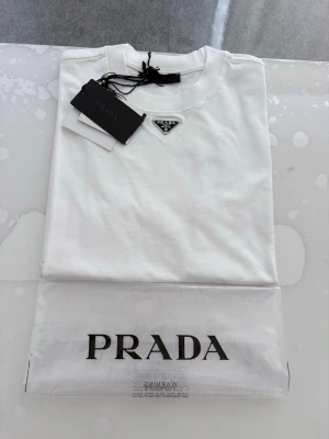 Prada T- shirt - Hej! Säljer en jätte fin T-shirt som är i väldigt bra skick inga problem alls Väldigt fin till sommaren Storlek S (lite baggy, kan även passa M) Påse och tags ingår Skriv gärna vid intresse ❤️💯