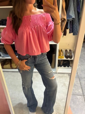 Rosa offshoulder blus - Trendig rosa offshoulder blus med smock upptill och vida puffärmar. Croppad modell som ger en avslappnad och cool vibe. Perfekt att matcha med jeans för en snygg och ungdomlig look. 
