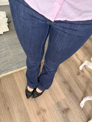 Mörkblå bootcut jeans - Säljer ett par mörkblå bootcut jeans med klassisk femficksdesign. Jeansen har en smal passform över låren och lätt utsvängda ben. Materialet är stretchigt denim som ger en bekväm känsla och snygg siluett.