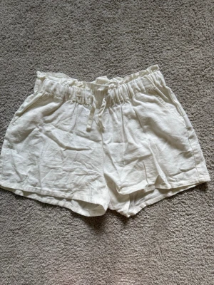 Vita linneshorts - Vita shorts i linne med avslappnad passform och resår i midjan. Shortsen har snören och två sidofickor, perfekta för varma dagar. Luftigt material och enkel design som passar till det mesta.