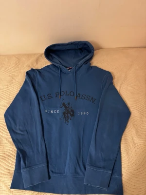 Blå hoodie från U.S. Polo Assn - Snygg blå hoodie från U.S. Polo Assn med tryck framtill och klassisk huva med dragsko. Perfekt för en avslappnad och sportig stil.