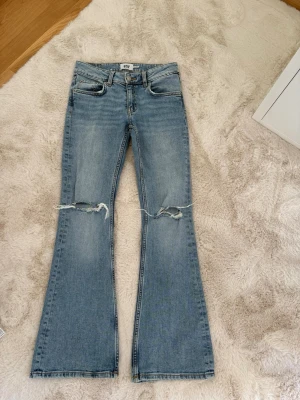 Ljusblå bootcut jeans med hål - Säljer dessa ljusblåa lågmidjade bootcut jeans ifrån lager 157. De är i storlek xs och längden short. De är använda fåtal gånger och har inga defekter!