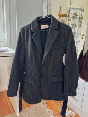 Mörkgrå oversized kavaj-jacka från Nelly - Mörkgrå oversized kavaj-jacka från Nelly med fiskbensmönster och tunna ljusa ränder. Snyggt oversized och perfekt till höst/vinter då tyget är åt tjockare hållet. Aldrig använd med prislapp kvar. 