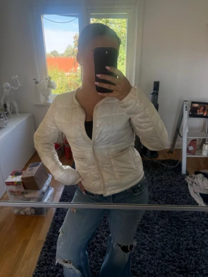 Vit pufferjacka med rund hals - Säljer en vit pufferjacka med rund halsringning och dragkedja framtill. Jackan har två fickor på sidorna och quiltad design. Passar perfekt till kalla dagar och har en clean, enkel look som är lätt att matcha.