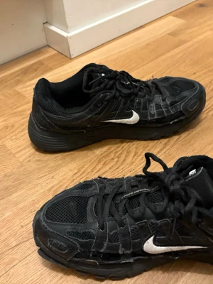 Svarta p6000 - Säljer ett par svarta Nike sneakers med vit swoosh på sidan. Skorna har mesh- och syntetpaneler, snörning och en chunky sula. Perfekta för dig som gillar sportig och street-inspirerad stil.