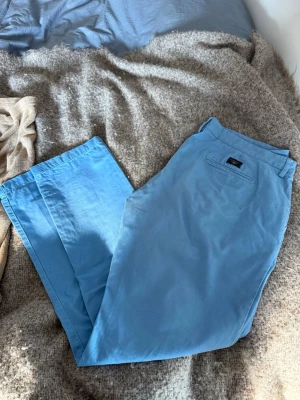 Ljusblå chinos från Gant - Snygga ljusblå chinos från Gant i klassisk rak modell. Byxorna har två sidofickor och en bakficka med Gant-logga ovanför. Tillverkade i mjukt bomullstyg som ger en skön känsla och stilren look.