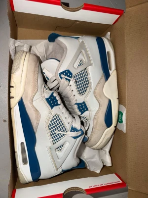 Vita och blå höga sneakers - Säljer ett par vita sneakers med blå detaljer och meshpaneler. Skorna har högt skaft, tjock sula och klassisk snörning. Materialet är en mix av läder och textil med ventilerande mesh på sidorna. Perfekta för dig som gillar retrostil och streetwear.
