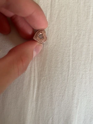 Roséguld hjärtberlock - Söt berlock i form av ett hjärta i roséguld med glittrande stenar runt kanten och ett litet hjärta i mitten. Perfekt att använda på armband eller halsband för en personlig touch.