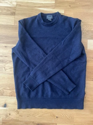 Mörkblå merinoull tröja från H&M - En enkel och stilren mörkblå stickad tröja från H&M. Tröjan har rund halsringning, långa ärmar och ribbade muddar vid ärmslut och nederkant. Perfekt att matcha med jeans eller kjol för en clean look.