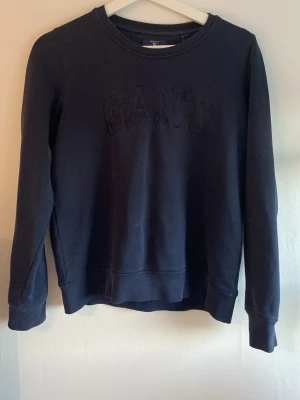 Mörkblå GANT sweatshirt - Mörkblå sweatshirt från GANT med broderad logga på bröstet. Tröjan har rund halsringning, långa ärmar och ribbade muddar vid ärmslut och nederkant. Tillverkad i mjukt material för en skön och avslappnad look.