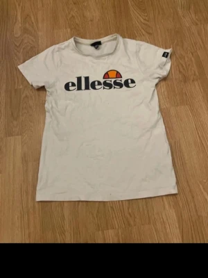 Vit ellesse t-shirt med logga - Vit t-shirt från ellesse med stor logga tryckt över bröstet. Klassisk rund halsringning och korta ärmar. Perfekt för en avslappnad och sportig stil. Tillverkad i mjuk bomull för skön känsla hela dagen.