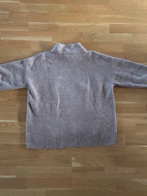 Beige stickad polotröja - Mysig beige stickad tröja med hög krage och avslappnad passform. Tröjan har ribbstickade muddar vid ärmslut och nederkant, vilket ger en snygg detalj. Perfekt för kalla dagar och enkel att matcha med jeans eller kjol.
