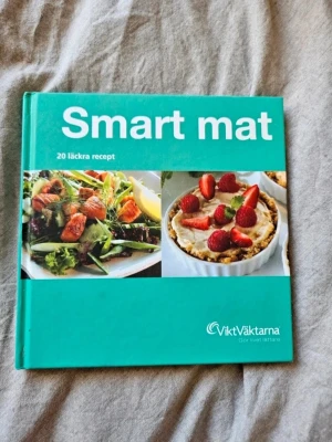 Smart mat - 20 läckra recept - En inspirerande kokbok från ViktVäktarna med 20 smarta och hälsosamma recept. Boken har ett turkost hårt omslag med bilder på fräscha maträtter och desserter. Perfekt för dig som vill laga god och nyttig mat.