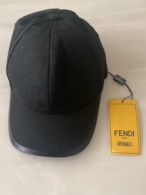 Svart keps från Fendi - Snygg svart keps från Fendi med klassisk böjd skärm och justerbart band bak. Kepsen har diskret struktur i tyget och Fendi-logga på insidan samt etikett. Perfekt accessoar för en trendig look.