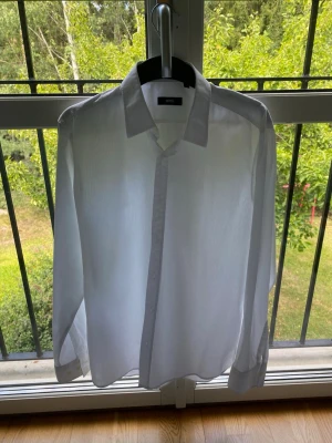 Vit skjorta från BOSS - Klassisk vit skjorta från Hugo Boss  i tunn bomull. Skjortan har lång ärm, knappar framtill och en stilren krage. Perfekt för en clean och fräsch look. Passar till många olika stilar och tillfällen.