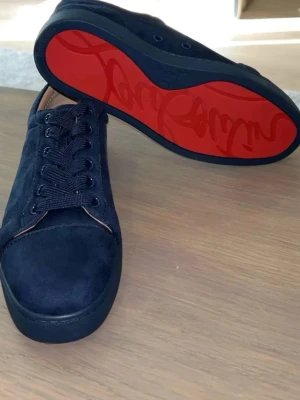 Christian Louboutin Skor - Snygga mörkblå sneakers från Christian Louboutin i mocka med klassisk röd sula och matchande mörkblå skosnören. Skorna har en stilren design och låg profil som ger en exklusiv känsla. Perfekta för dig som vill sticka ut med en ikonisk detalj.