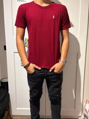 Vinröd t-shirt från Ralph Lauren - Snygg vinröd t-shirt från Ralph Lauren med klassisk passform och rund halsringning. Liten vit logga broderad på bröstet. Tillverkad i mjukt bomullsmaterial som känns skönt mot huden. Perfekt till jeans eller shorts för en clean och enkel stil.