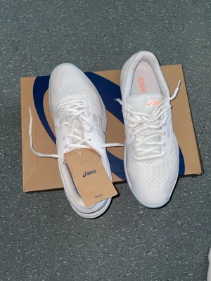 Vita Asics sneakers med meshdetaljer - Snygga vita sneakers från Asics med klassisk logga på sidan. Ovandelen är i mesh och syntet för bra andningsförmåga. Skorna har vita snören, diskreta detaljer i ljusblått och orange på sulan samt en bekväm, vadderad insida.