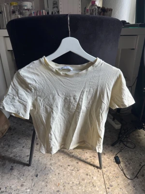 Ljusgul basic croppad t-shirt  - En enkel och stilren ljusbeige t-shirt i mjuk bomull. T-shirten har rund halsringning och korta ärmar, perfekt för en avslappnad look. Passar till det mesta och är ett måste i garderoben. Skulle säga att den sitter som xs!