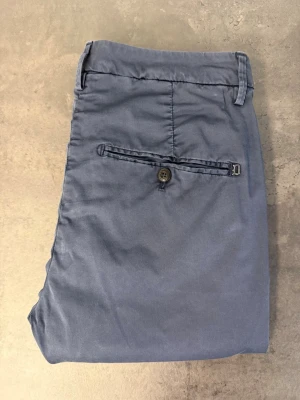 Mörkblå chinos från Dondup, W32 - Snygga mörkblå chinos med smal passform och klassiska fickor både fram och bak. Byxorna har bälteshällor och stängs med knapp och dragkedja. Tillverkade i ett mjukt bomullstyg som ger en skön känsla hela dagen.