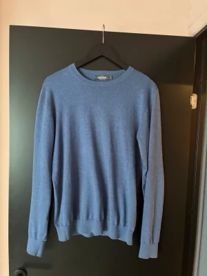 Dressman tröja  - En stilren blå tröja med rund halsringning och långa ärmar. Tröjan har ribbade muddar vid ärmslut och nederkant, vilket ger en snygg passform. Perfekt för lager på lager och enkel att matcha med olika outfits. Nån fläck men syns inte vid användning 