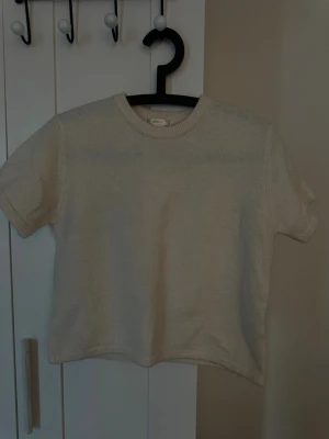 Vit stickad topp från Gina Tricot - Mysig vit stickad topp från Gina Tricot med rund halsringning och korta ärmar. Perfekt till både jeans och kjol för en enkel och clean look. Materialet är mjukt och ger en avslappnad känsla.