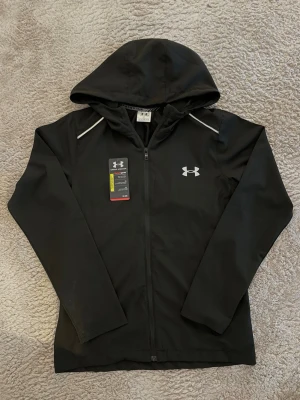 Under Armour Jacka - Svart Under Armour jacka/vindjacka helt ny i storlek M, men passar som S. Kommer med ddustbag och tags. Säljer på grund av att jag köpte fel storlek 