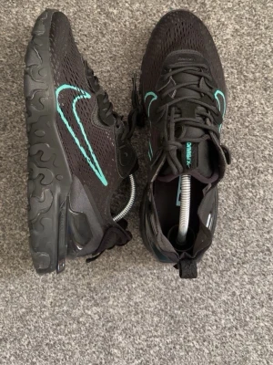 Svarta sneakers med turkos detalj - Snygga svarta sneakers med turkosa detaljer och en stor turkos swoosh på sidan. Ovandelen är i mesh för bra andningsförmåga och sulan har ett vågigt mönster för extra grepp. Skorna har snörning och en modern, sportig look.