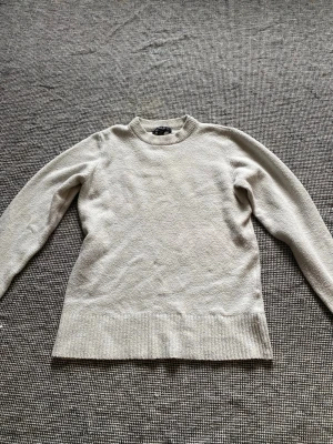 Beige stickad tröja med rund hals - En enkel och stilren beige stickad tröja med rund halsringning och långa ärmar. Tröjan har ribbstickade muddar vid ärmslut och nederkant. 